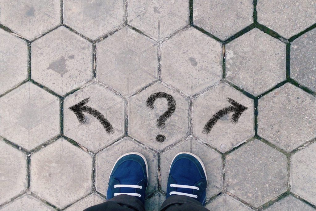top view of blue shoes on tiled pavement with question mark and two arrows, concept of career crossroads